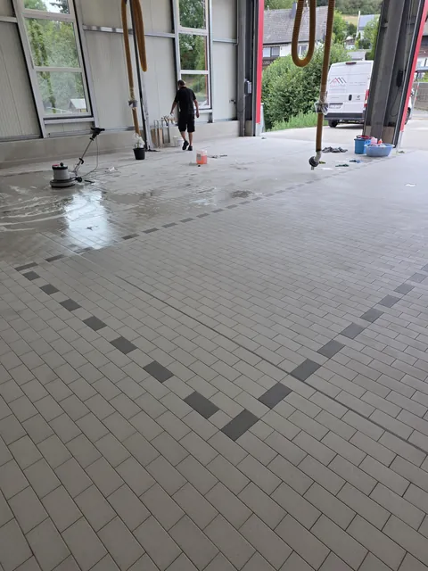 Laufende Reinigung des gefliesten Hallenbodens mit Reinigungsflotte und Einscheibenmaschine