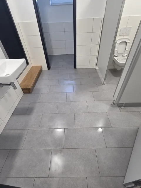 Gereinigter Fliesenboden im Sanitärbereich mit Waschplatz und WC-Kabinen